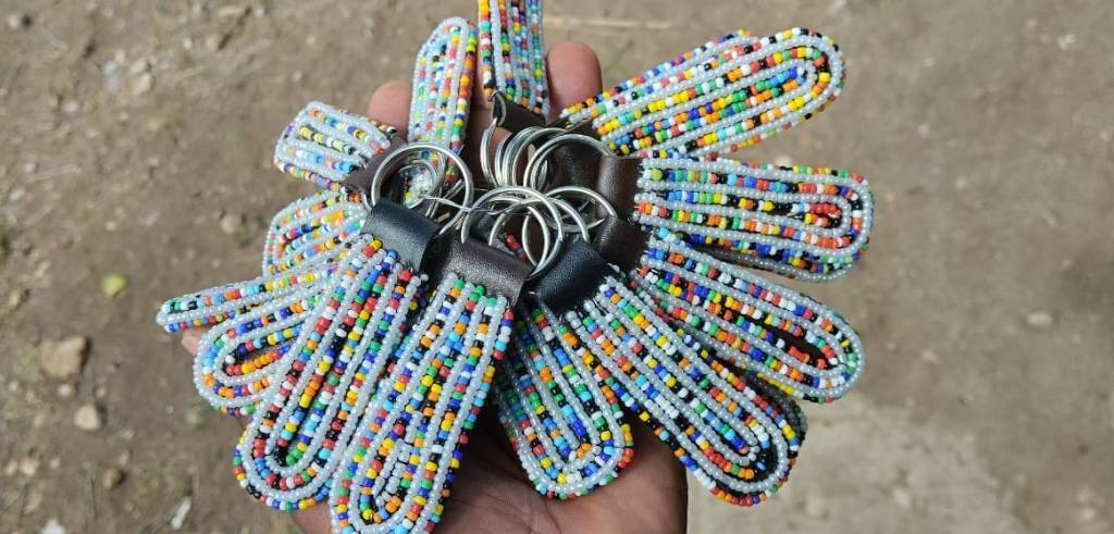 Hand håller en bunt med handgjorda nyckelringar gjorda av färgglada pärlor.