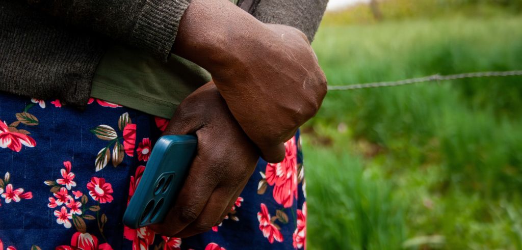 Händer som håller en mobiltelefon framför ett blomstrande förkläde.